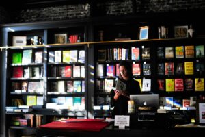 Bookstore cashier reading behind the counter in front of tall shelves of books