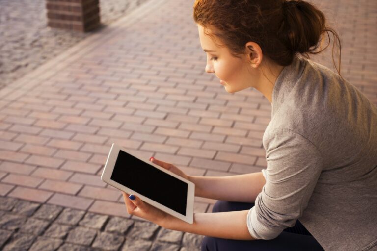 Woman sitting on a brick walkway reading on an iPad